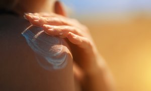 Frau die sich die Schulter mit Sonnencreme eincremt
