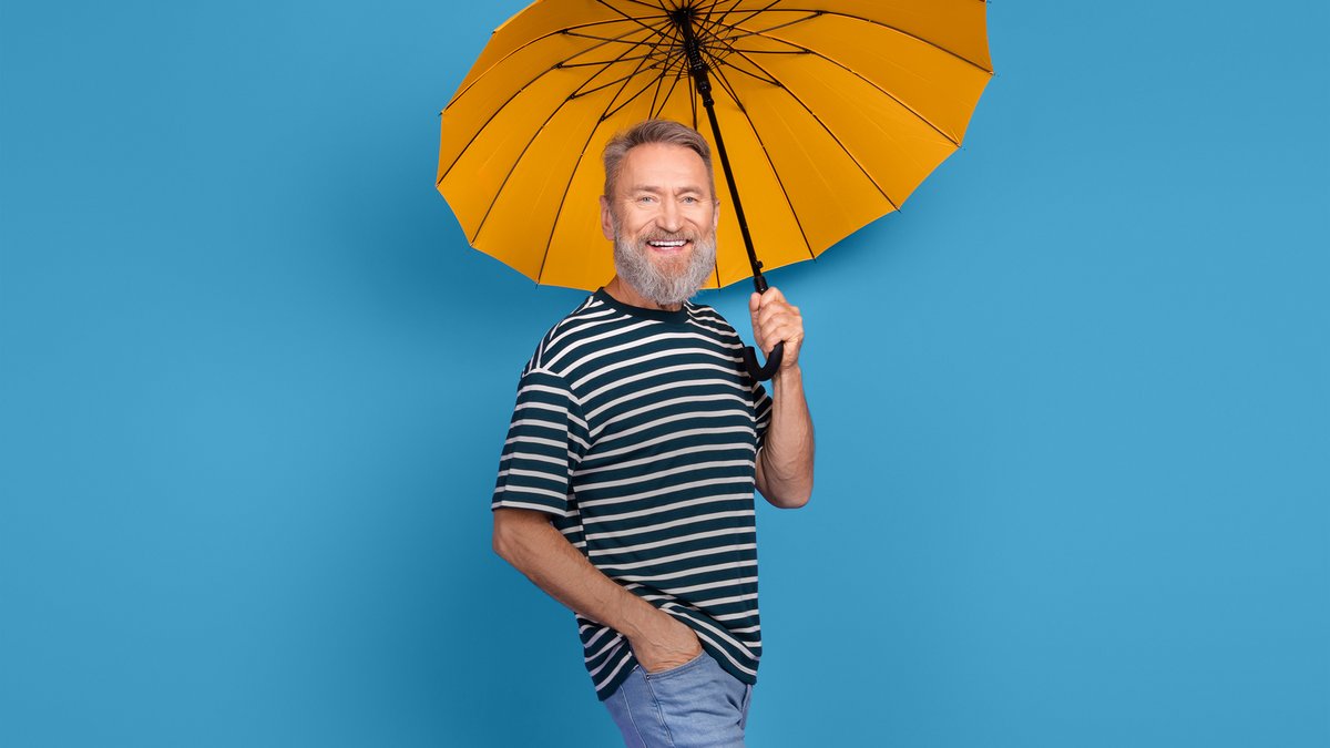 Lachender Mann mittleren Alters mit grauem Bart unter einem orangefarbenen Regenschirm