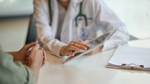 Arzt im Patientengespräch am Tisch mit Tablet in der Hand