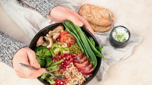 Person hält eine Schüssel voll mit gesundem Essen wie Bohnen, Tomaten, Broccoli, und Vollkornreis in den Händen