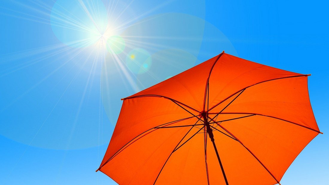 Sonne scheint von blauem Himmel auf organgefarbenen Regenschirm