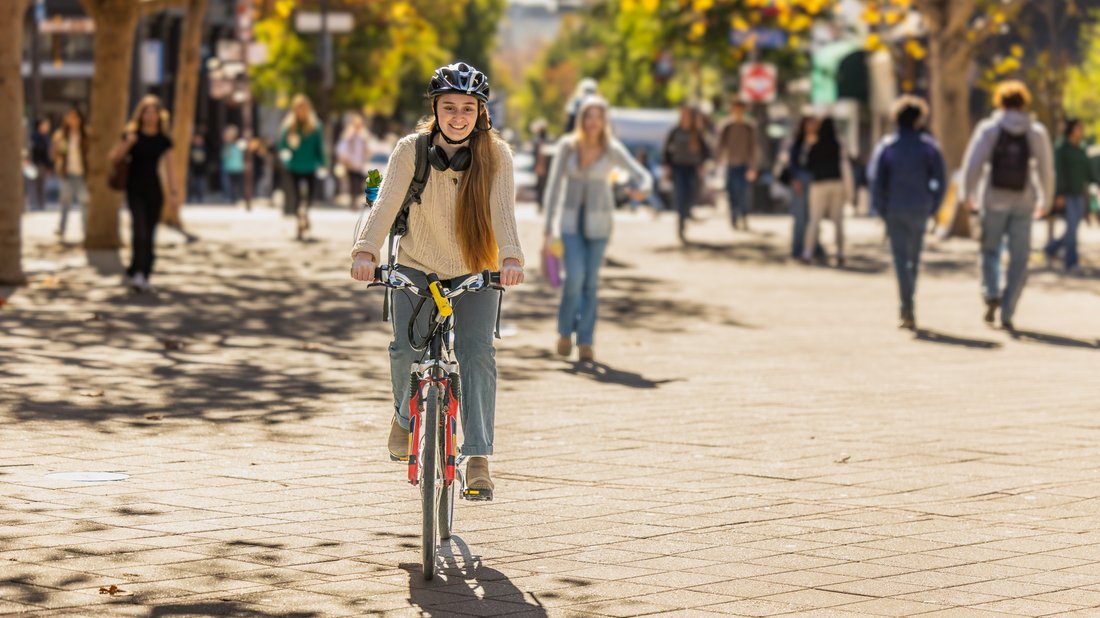 Radfahrerin und Fußgänger in einem herbstlichen Park bei Sonnenschein