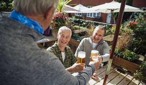 Drei ältere Männer im Biergarten, die sich anlachen und sich mit Bier zuprosten