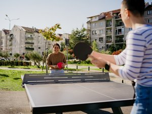 Zwei lachende Frauen die im Sonnenschein in einer Wohnsiedlung Tischtennis spielen