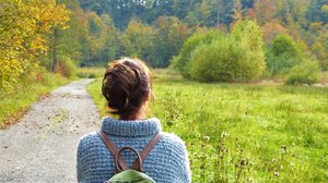 Frau mit Wollpullover und Rucksack auf einem Weg in herbstlicher Natur