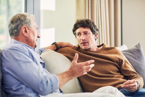 Ein älterer und ein jüngerer Mann sitzen sich auf der Couch gegenüber und unterhalten sich