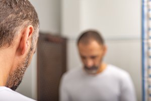 Mann mit kurzen grauen Haaren und Bart vor Spiegel