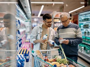 Älterer und jüngerer Mann mit gefülltem Einkaufswagen im Supermarkt bei Auswahl von Produkten