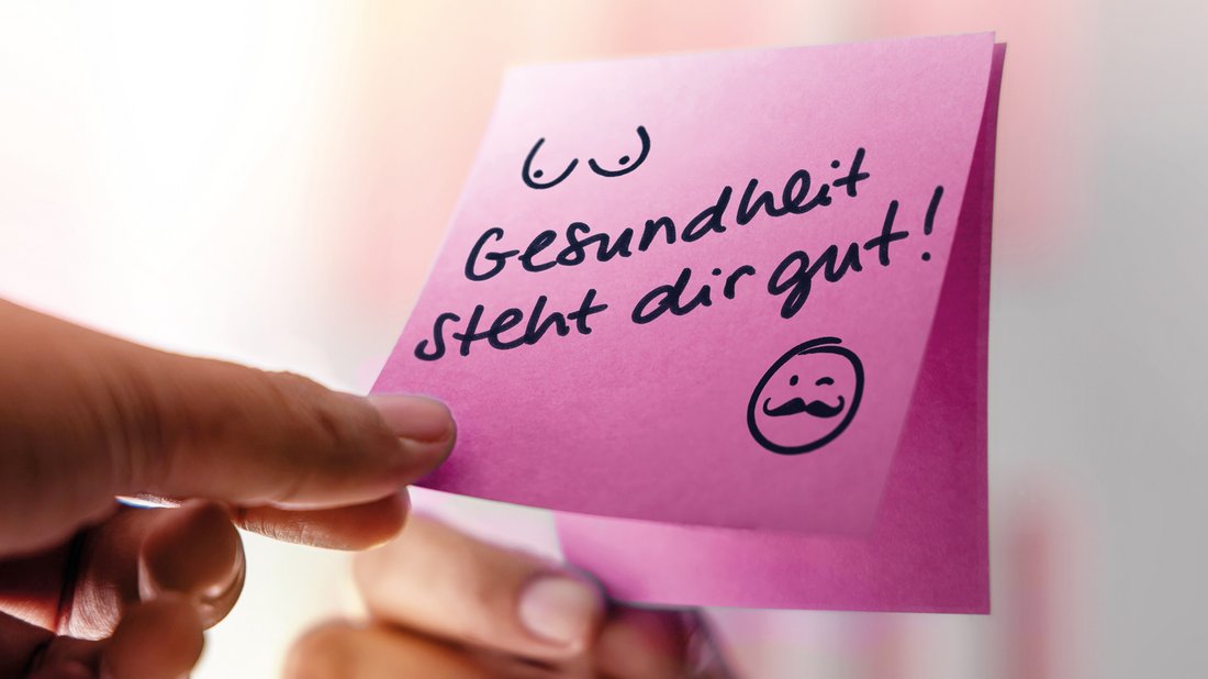 Finger halten pinkfarbenes Post-it mit Text "Gesundheit steht dir gut" am Spiegel