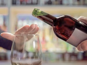 Person hält Hand über ein Weinglas und lehnt den angebotenen Wein ab