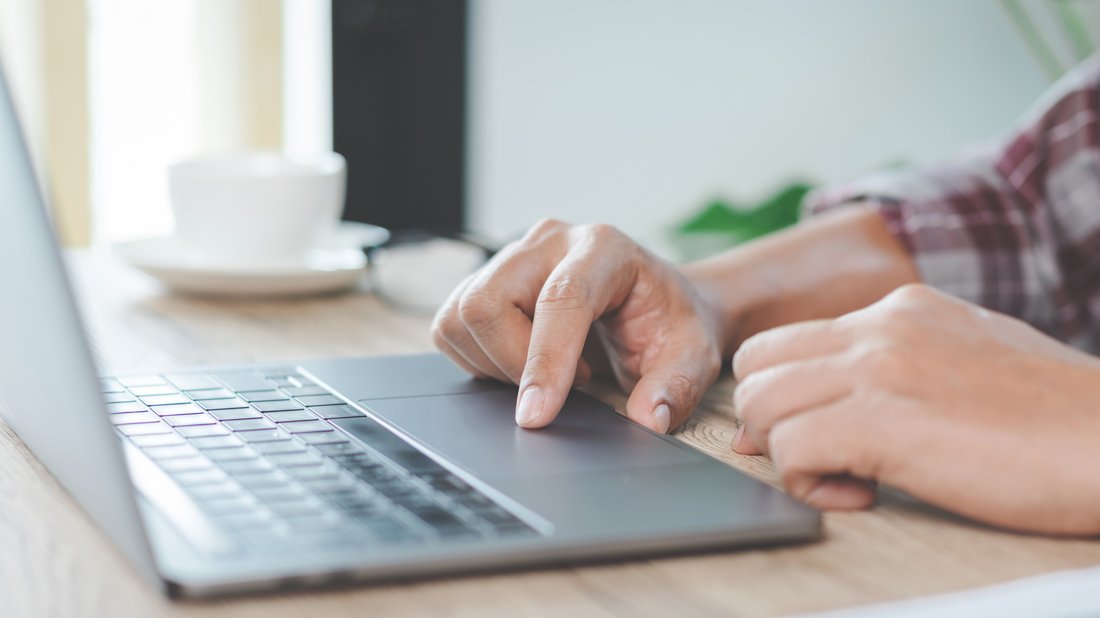 Person am Laptop mit Kaffeetasse im Hintergrund