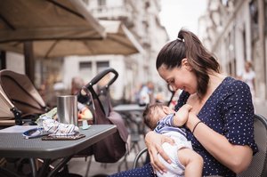 Frau sitzt im Außenbereich eines Cafés und stillt ihr Baby